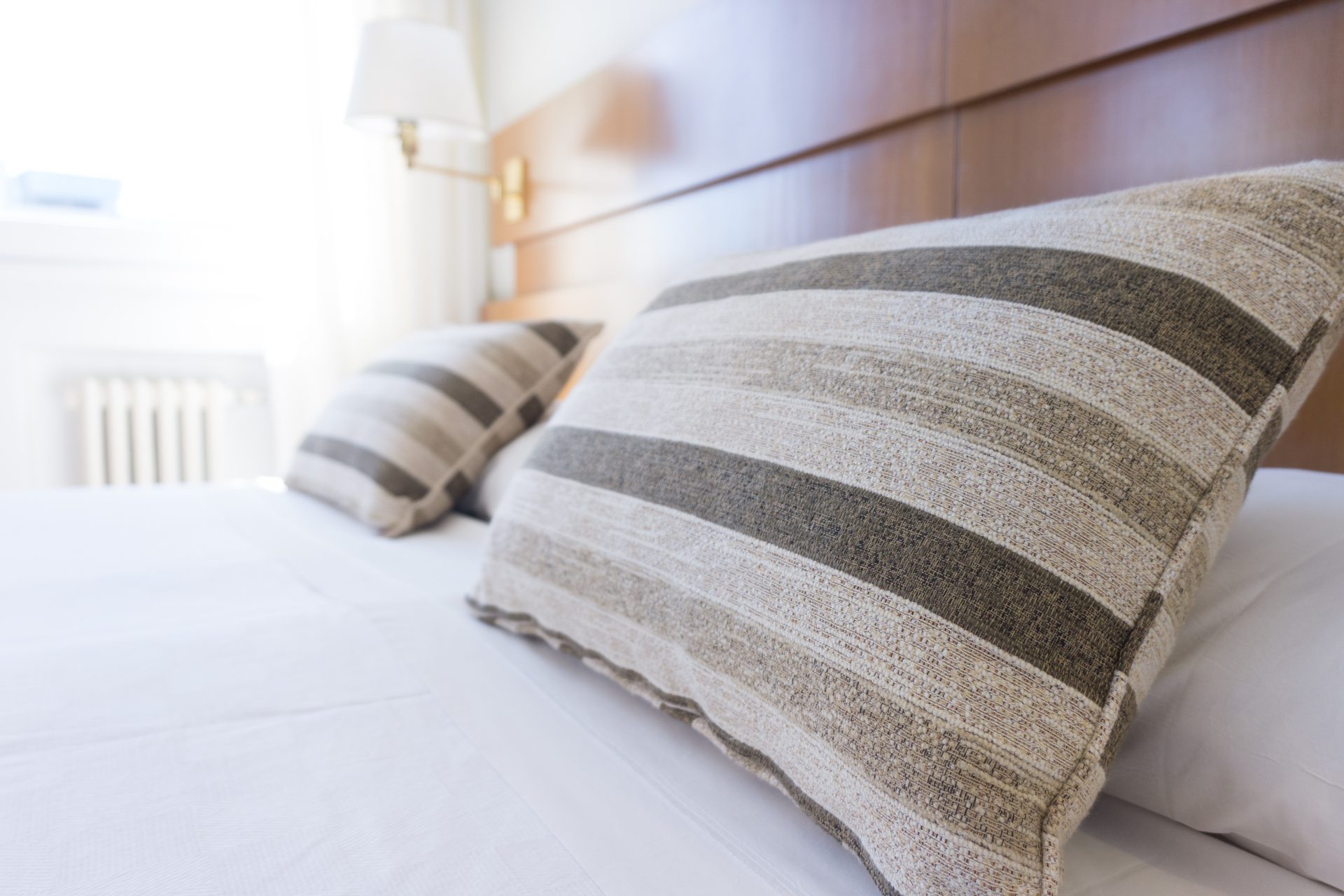 A nicely made hotel bed with white linen and striped pillow covers